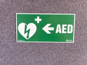 tabliczka informacyjna na ścianie przy wejściu do portierni z napisem AED