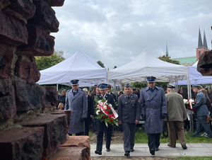 delegacja złożona z 2 policjantów i 2 innych mundurowych idą pod pomnik złożyć wiązankę kwiatów