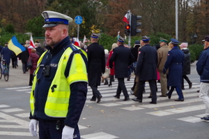policjant kieruje ruchem podczas przemarszu kolumny uczestników uroczystości przez przejście dla pieszych