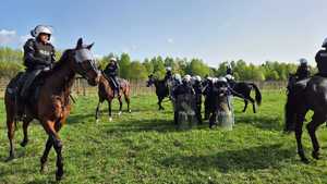 Policjanci na koniach ćwiczą posłuszeństwo, a umundurowani policjanci uderzają pałkami w tarcze nadając podobne dźwięki wydobywające się podczas zabezpieczenia meczu