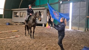 Policjantka wymachuje flaga przed koniem, który pokonuje tor ze swoim jeźdźcem