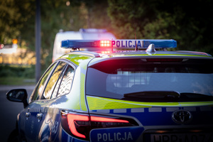 zdjęcie radiowozu z włączonymi sygnałami błyskowymi, zrobione od tyłu.