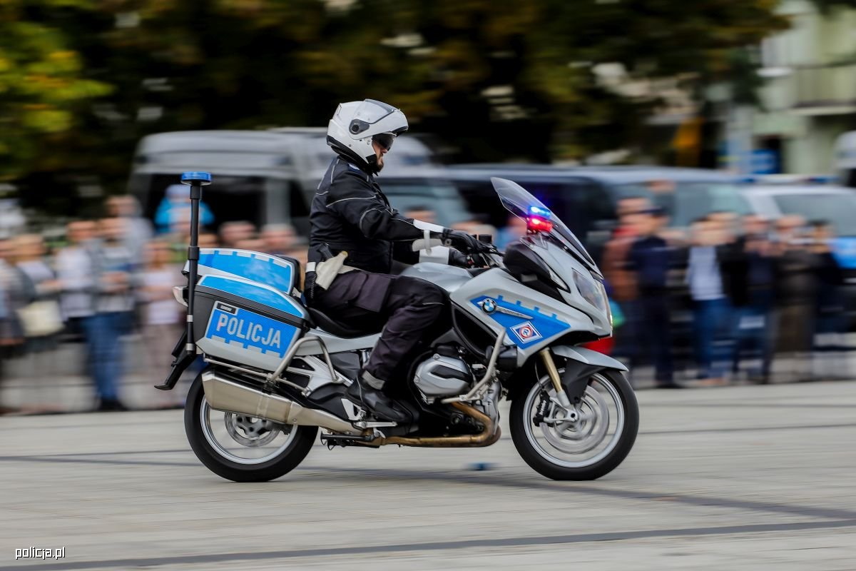 Zdjęcie przedstawia policyjnego motocyklistę w ruchu ulicznym.