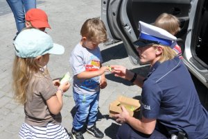 Spotkanie policjantów z przedszkolakami, policjantka wręcza dzieciom odblaski.