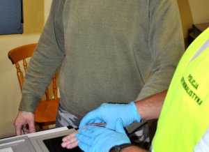 Policjant daktyloskopuje zatrzymanego.