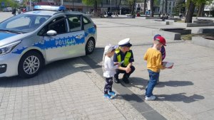 policjantka kuca przy dzieciach w tle radiowóz