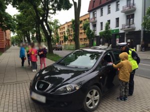 policjantka w mundurze z dziećmi ze szkoły wręczają laurki kierowcy i romzawiają o przestrzeganiu przepisów