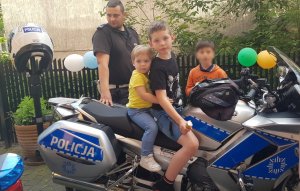 policjant stoi przy motocyklu, na którym siedzi dwóch chłopców