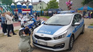 policjanci na motocyklach i radiowozem na festynie. w tle widać wiele osób uczestników festynu