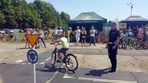 policjant w mundurze na miasteczku rowerowym przygląda się dzieciom jeżdżącym na rowerach