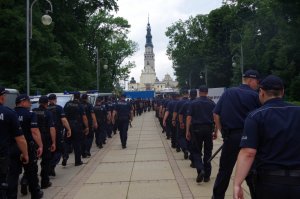 Policjanci tyłem do fotografującego w dwóch rzędach idą w kierunku Jasnej Góry