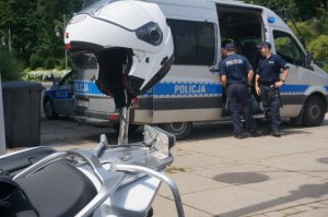 kask motocyklowy na pierwszym planie, w tle policyjnby radiowóz z dwoma policjantami przy nim