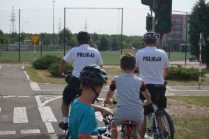 dwóch policjantów na rowerach jeździ po miasteczku rowerowym z dziećmi na rowerach