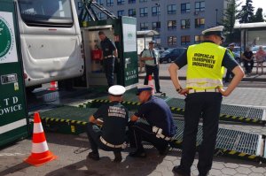 policjanci kucają przy platformie mobilnej stacji kontroli pojazdów, na której stoi na podwyższeniu kontrolowany autobus