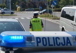 na pierwszym planie sygnały świetlne na radiowozie policji, w tle policjantka przy drodze