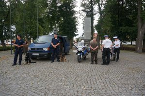 policjanci ruchu drogowego na motocyklach i przewodnicy psów na tle parku w Koniecpolu rozmawiają z mieszkańcami
