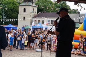 Komendant Miejski Policji przez mikrofon na scenie informuje obywateli o zagrożeniach związanych z oszustwami pod tzw. legendą