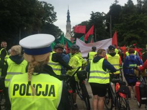 policjantka ruchu drogowego skierowana w stronę Jasnej Góry przed nią pielgrzymka rowerzystów w tle wieża jasnogórska