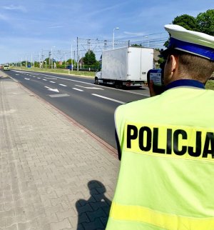 policjant przy drodze w rękach trzyma miernik prędkości i mierzy prędkość przejeżdżających samochodów