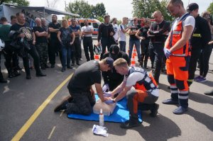 mężczyzna ćwiczący reanimację na manekinie, obok ratownicy medycznie, dookoła ustawieni ludzie