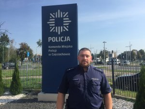 dzielnicowy pozuje do zdjęcia na tle banneru Komendy Miejskiej Policji w Częstochowie