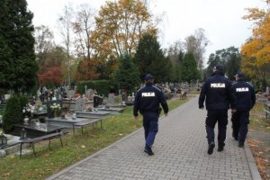3 policjantów idzie po alejce na cmentarzu