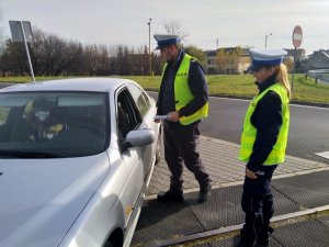 policjant i policjantka stoją przy drzwiach samochodu i rozmawiają przez uchylona szybę z kierującym