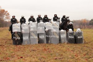 policjanci z pododdziału policyjnego z tarczami, za nimi policyjni jeżdźcy na koniach