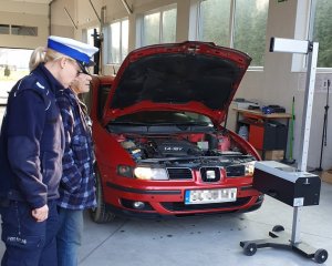 samochód z otwartą maską obok policjantka i pracownik stacji diagnostycznej