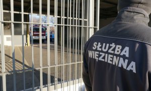 strażnik więzienny w tle wjeżdżajacy przez bramę aresztu radiowóz straży pożarnej