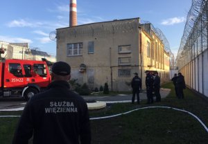 strażnik więzienny w tle radiowóz straży pozarnej przy budynku, obok policjanci i straż więzienna