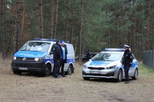 dwa radiowozy ustawione na polanie leśnej obok policjanci