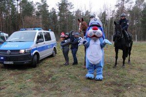 sznupek, dwóch jeżdźców konnych na rumakach, radowóz oraz dzieci