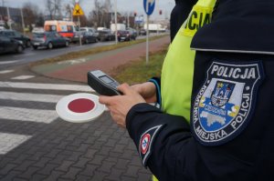 rękaw munduru, w tle ręka policjanta, który trzyma tarczę do zatrzymywania pojazdów i alcosensor do badania stanu trzeźwości