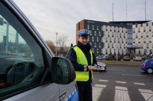 policjant obok radiowozu, w tle budynek komendy