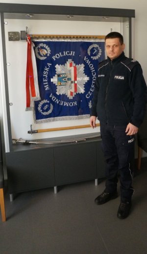 policjant w mundurze na tle sztandaru Komendy Miejskiej w Czestochowie