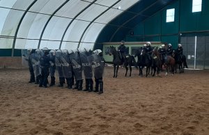 policjanci z SPPP i policjanci na koniach w obiekcie zadaszonym w stadninie koni podczas ćwiczeń