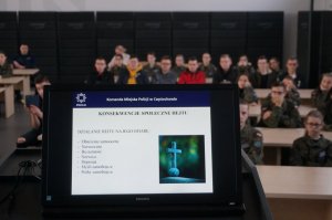 monitor z wyświetlanym podczas prelekcji slajdem, w tle zgromadzona młodzież - uczniowie klas mundurowych