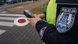 policjant trzyma w dłoni tarczę do zatrzymywania pojazdów w tle przejście dla pieszych