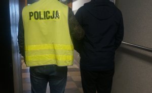 policjant w kamizelce odblaskowej prowadzi zatrzymanego