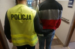 policjant w kamizelce odblaskowej stoi obok zatrzymanego tyłem na korytarzu