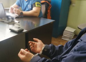 zatrzymany siedzi na krześle, w tle za biurkiem policjant