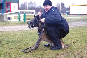 policjant z psem służbowym w kagańcu pokazuje palcem znak okay