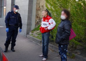 policjanci legitymują mężczyznę bez maseczki i kobietę w maseczce, zakrywającej usta i nos