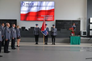 policyjny sztandar i poczet sztandarowy stoi na środku auli podczas uroczystości w Komendzie