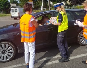 policjantka informuje kierowcę o zagrożeniach związanych z nieprzestrzeganiem przepisów w rejonie przejazdu kolejowego i rozdaje ulotki