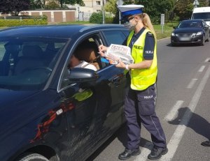 policjantka informuje kierowcę o zagrożeniach związanych z nieprzestrzeganiem przepisów w rejonie przejazdu kolejowego i rozdaje ulotki