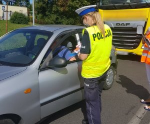 policjantka informuje kierowcę o zagrożeniach związanych z nieprzestrzeganiem przepisów w rejonie przejazdu kolejowego i rozdaje ulotki