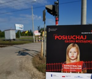 plakat z napisem akcji ustawiony przed przejazdem kolejowym