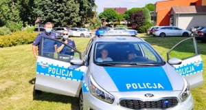 policjanci przy oznakowanym radiowozie rozmawiają z dorosłymi i rozdają dzieciom odblaski